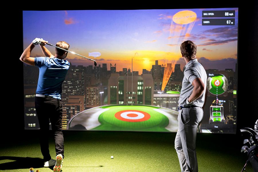 Two golfers playing in a simulator bay
